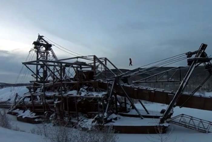 Jovem anda em corda bamba em máquina abandonada na neve
